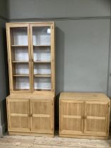 A cabinet in American pine having two glazed doors with interior shelves above two indented panel