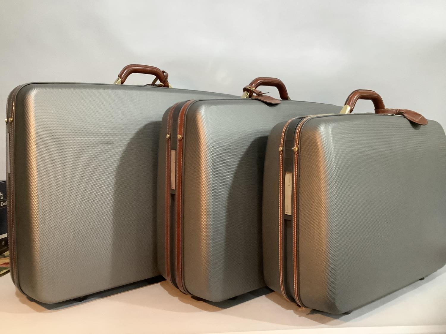 Three Samsonite hard shell grey and leather suitcases with pull-along handles and wheels