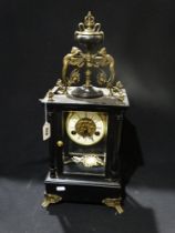 An Ebonized Mantel Clock With Circular Dial & Visible Movement, The Case Mounted With Cherubs
