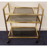 1970s TROLLEY with a brushed yellow steel frame with three smoked glass shelves, on casters, 77cm