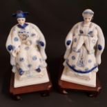 PAIR OF PORCELAIN ASIAN FIGURINES depicting a seated emperor and empress, on hardwood stands, 20.5cm