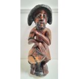 CARVED TEAK CARIBBEAN FIGURE depicting a man wearing a hat seated with a drum, 70cm high