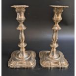 PAIR OF GEORGE V SILVER CANDLESTICKS with knopped stems and raised on shaped square bases, with