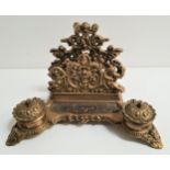 ORNATE BRASS DESK STAND with a rear letter rack decorated with putti, with two circular lidded