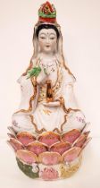 PORCELAIN FIGURINE GUANYIN seated with crossed legs on a lotus leaf base, holding a gilt urn and a