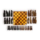 An African carved hardwood chess set, modelled as figures, with natural wood and ebonised pieces,