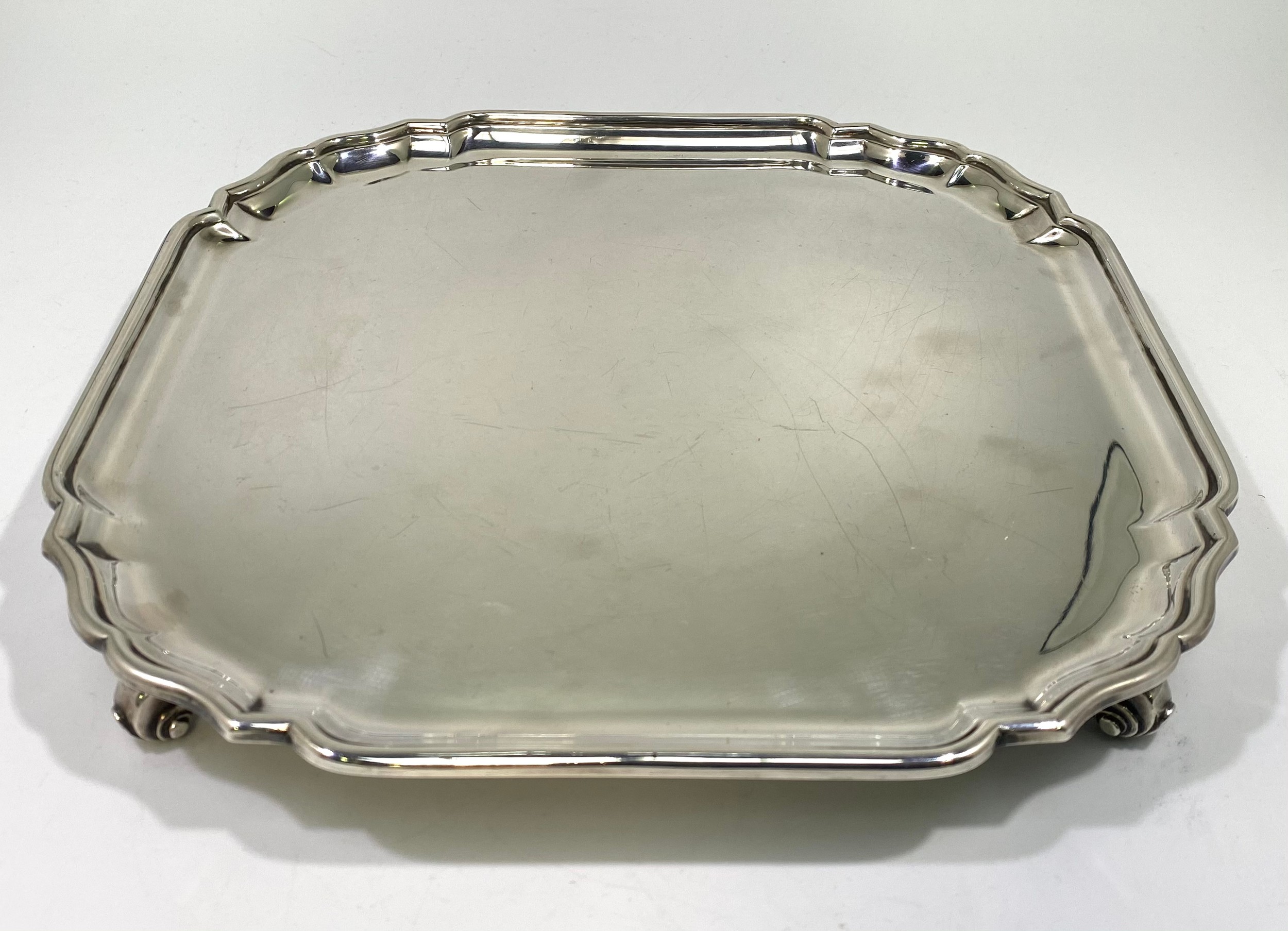 A ERII silver salver of square form with serpentine canted corners, pie-crust rim raised on four