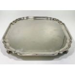 A ERII silver salver of square form with serpentine canted corners, pie-crust rim raised on four