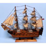 A wooden model of H.M.S Victory rigged in full sail, raised on base, measures 51cm long, together