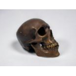 A cast and patinated bronze model of a human skull, with hinged jawbone, 19x15x12cm