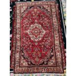 A Persian hand-knotted wool rug, worked with a central stylised floral medallion to a red ground,