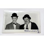 A monochrome real photographic postcard of Laurel & Hardy, signed in blue ink by Oliver Hardy, 140mm