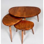 A nest of three blonde elm Ercol pebble tables, raised on splayed and turned beech supports, largest