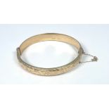 A 9ct yellow gold hinged bangle with safety chain, engraved to the front, with plain back, weighs