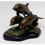 A patinated cast bronze figure group of three leaping dolphins on the crest of a wave, on plinth