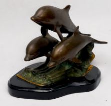 A patinated cast bronze figure group of three leaping dolphins on the crest of a wave, on plinth