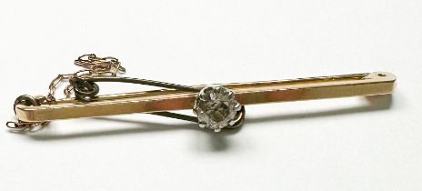 A 9ct yellow gold bar-brooch with safety chain, claw set with a solitaire diamond to the centre,