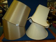 A pair of large gold coloured lampshades and two large cream lampshades.