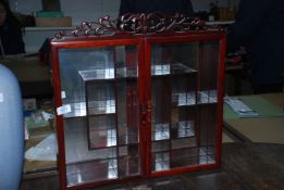 An Oriental style wall hanging display cabinet with mirror back and glazed doors and eleven