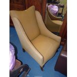 A brown upholstered pre 1950 fireside armchair having brief front cabriole legs and brass castors.