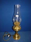 A brass finished Oil lamp converted to electric with clear glass chimney, 24" tall overall.