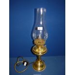 A brass finished Oil lamp converted to electric with clear glass chimney, 24" tall overall.