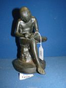 A well-modelled bronze figure depicting an athletic young man seated cross-legged on a stump