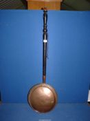 A copper warming pan with ebonised wooden handle.