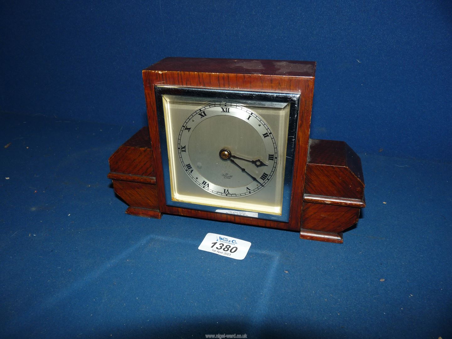 An oak cased Art Deco design square faces mantel clock having silvered chapter ring with Roman