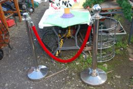 Two chrome barrier stands with red rope.