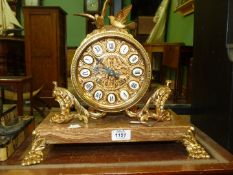 A brass Mantle Clock on a brown marble base having brass bunch of grapes style feet,