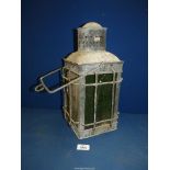 An old metal Lamp with green glass panels enclosed on a protective grid frame, with swing handle,