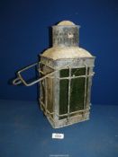 An old metal Lamp with green glass panels enclosed on a protective grid frame, with swing handle,