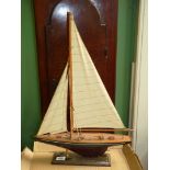 A wooden model of sailing yacht with blue and mauve hull, mounted on wooden plinth,