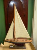 A wooden model of sailing yacht with blue and mauve hull, mounted on wooden plinth,