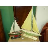 A wooden model of a sailing yacht with pale green hull and yellow sails, mounted on wooden plinth,