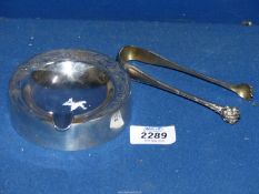 A continental silver lion paw sugar tongs, marked 800 and a 925 circular ashtray with wooden base.
