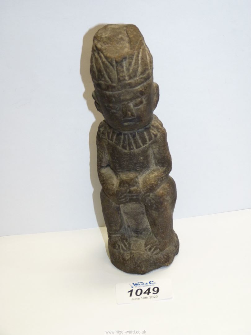 A Stone carved figure of a seated man with clasped hands, wearing head piece and collar, 7" tall.