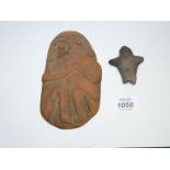 A flat piece of terracotta in the form of a seated person clasping their hands,