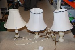 Three table lamps with marble effect bases and cream shades.