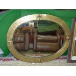 A wall mirror, oval shaped with textured brass frame having Fleur de lys detail and bevel edge,