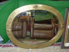 A wall mirror, oval shaped with textured brass frame having Fleur de lys detail and bevel edge,