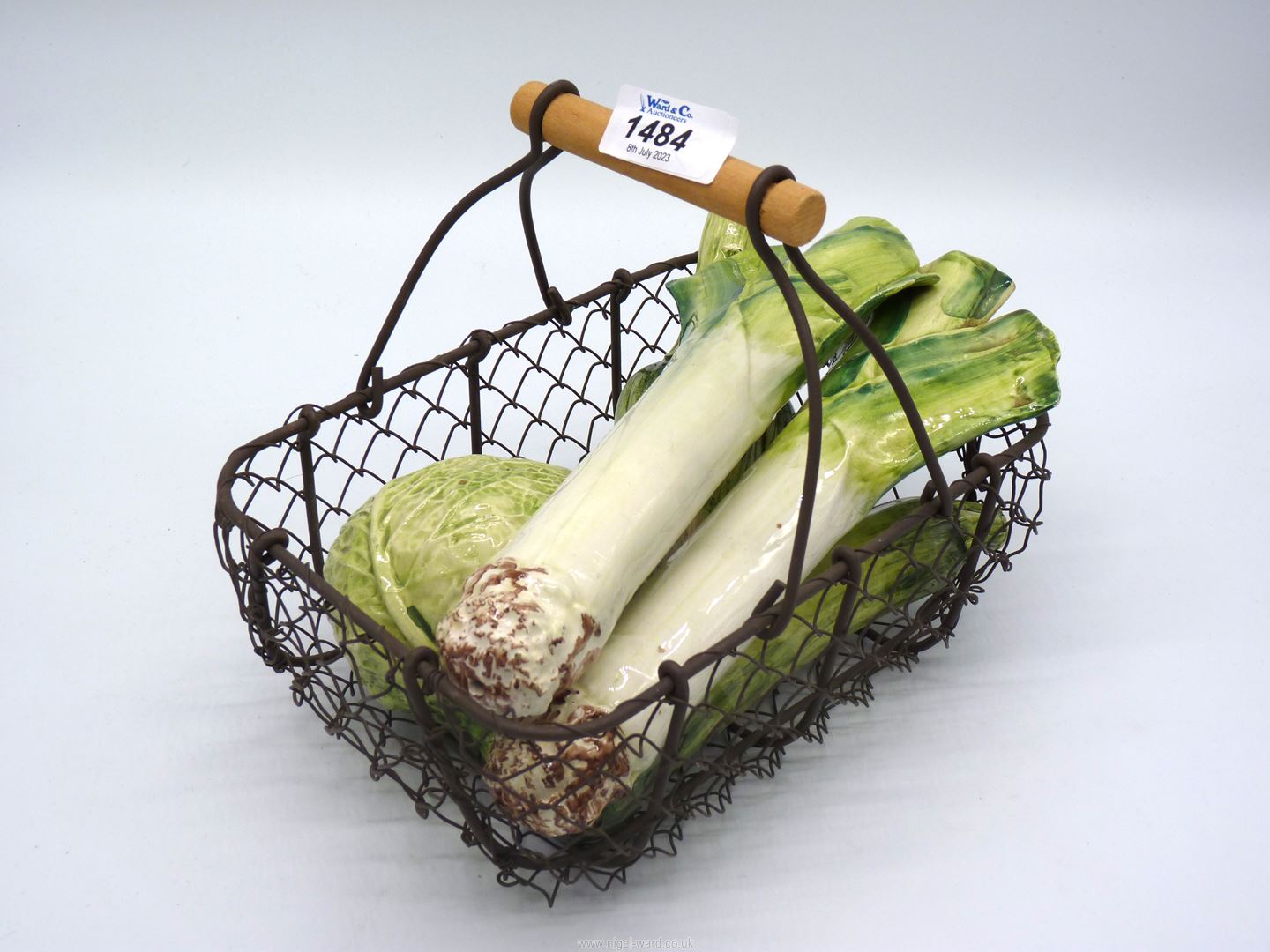 A small metal mesh basket of china vegetables including two leeks, Savoy cabbage,
