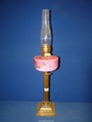 An Oil lamp on brass square base with reeded column supporting a pink glass reservoir with floral