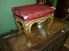 A giltwood and gesso framed stool, the frieze and legs decorated with scrolls and flower blooms,