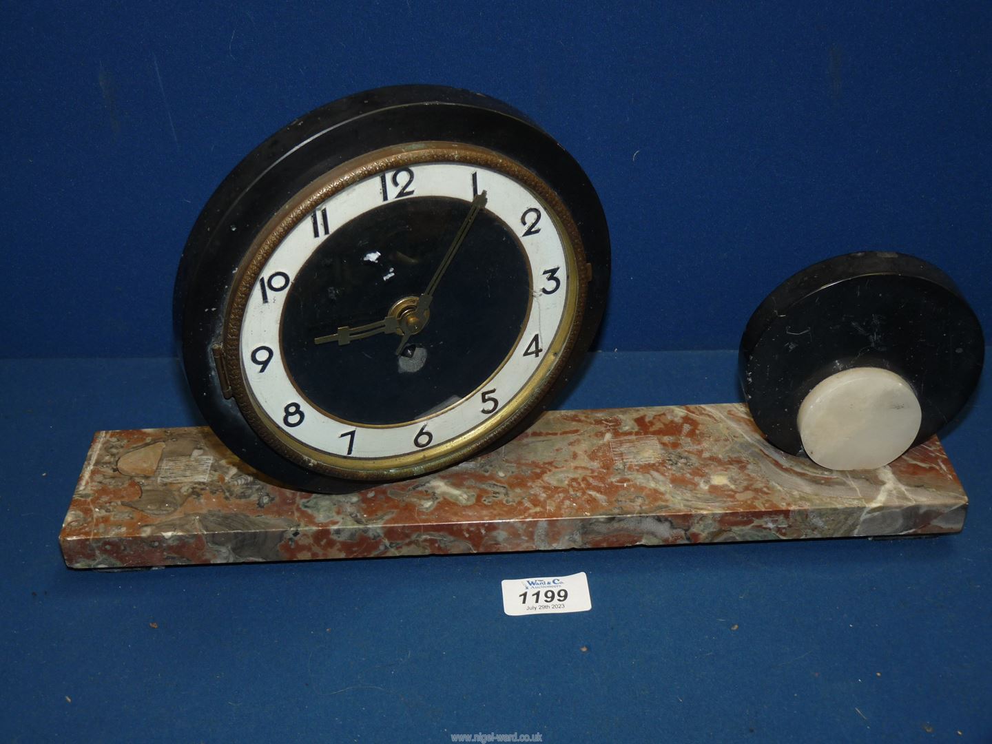 A circular Art Deco mantle clock with Arabic numerals and off set mounted on a red marble plinth