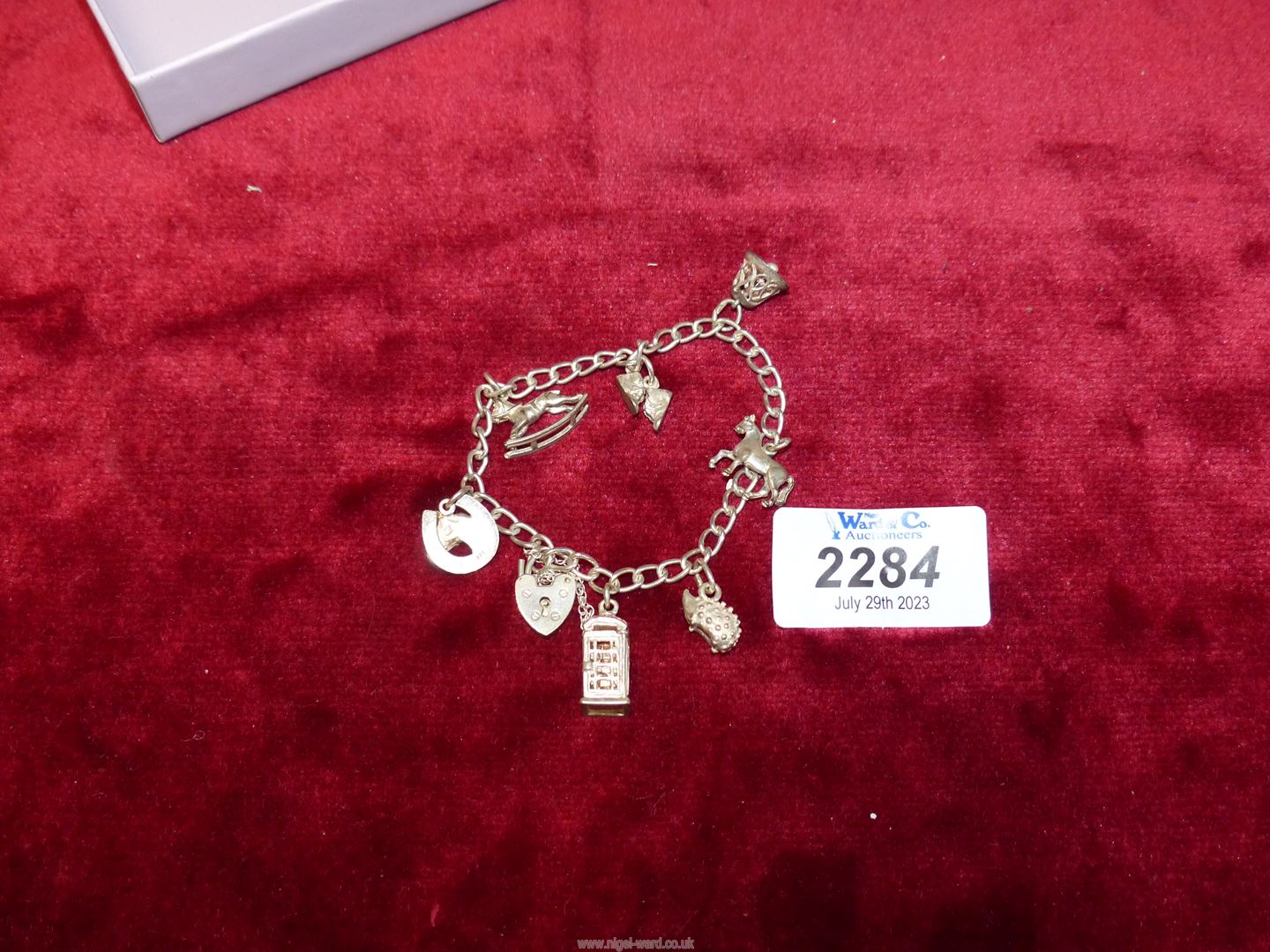 A silver charm bracelet with heart padlock clasp, charms including telephone kiosk, hedgehog, bell,