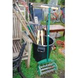 A black plastic dustbin containing garden tools, draining rods, bow saw, and lawn aerator.