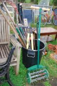 A black plastic dustbin containing garden tools, draining rods, bow saw, and lawn aerator.