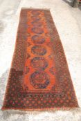 An Afghan bordered pattern and fringed runner in orange and navy with eight medallions, 10' x 35".